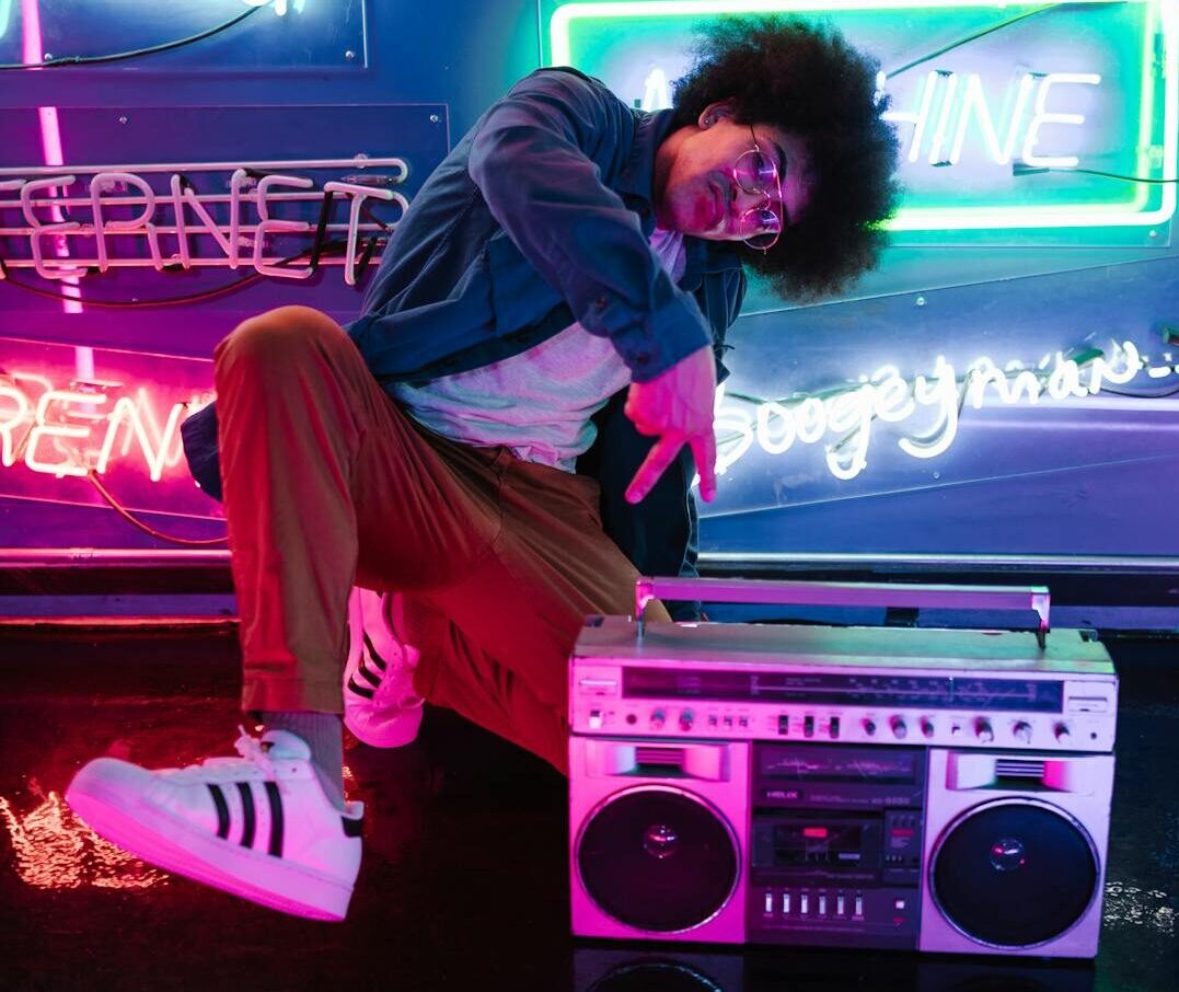 Stylish man poses with a retro boombox in a vibrant neon-lit club scene, evoking a cool nightlife vibe.