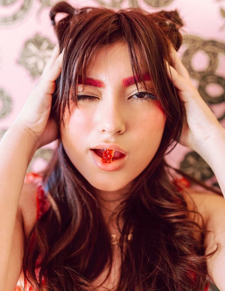 A young woman with bold red makeup and unique hairstyle poses vibrantly, capturing a fresh and stylish look.