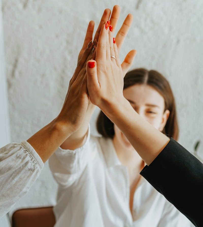 A group of adults in a warm atmosphere celebrating teamwork with a high-five gesture.